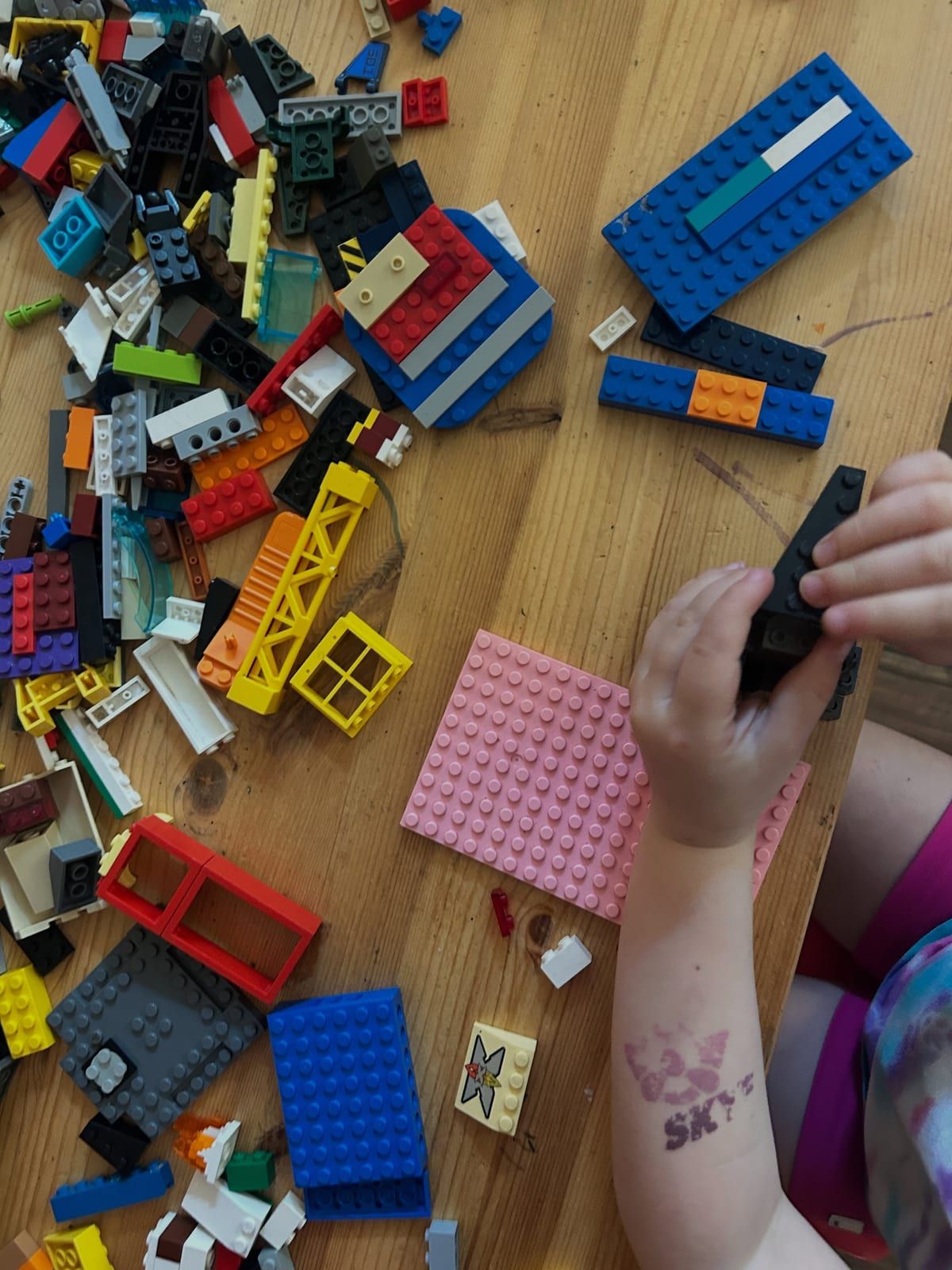 Hands building with a pile of colorful toy bricks on a wooden table.