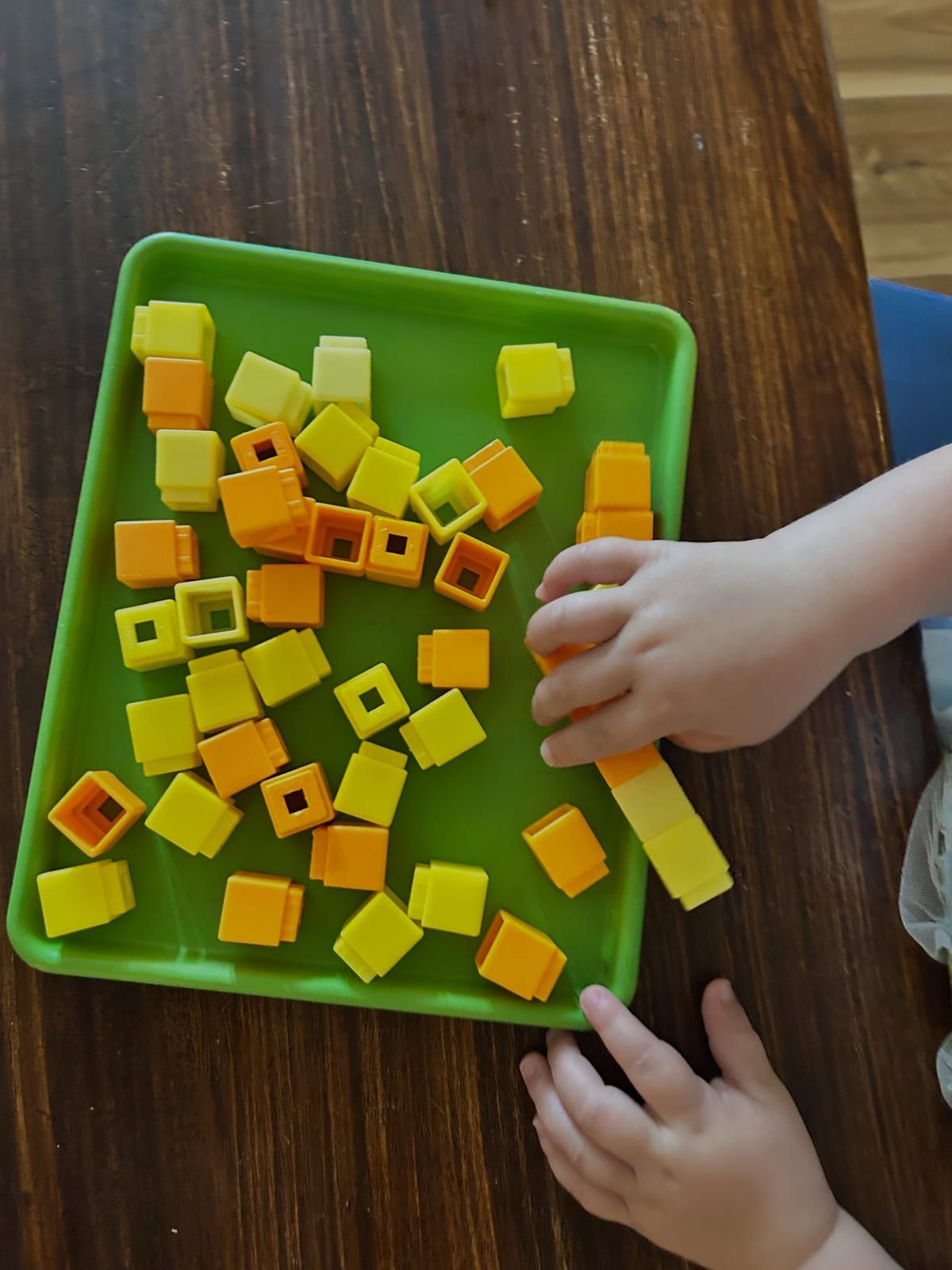 A child's hands arranging yellow and orange cubes on a green tray.