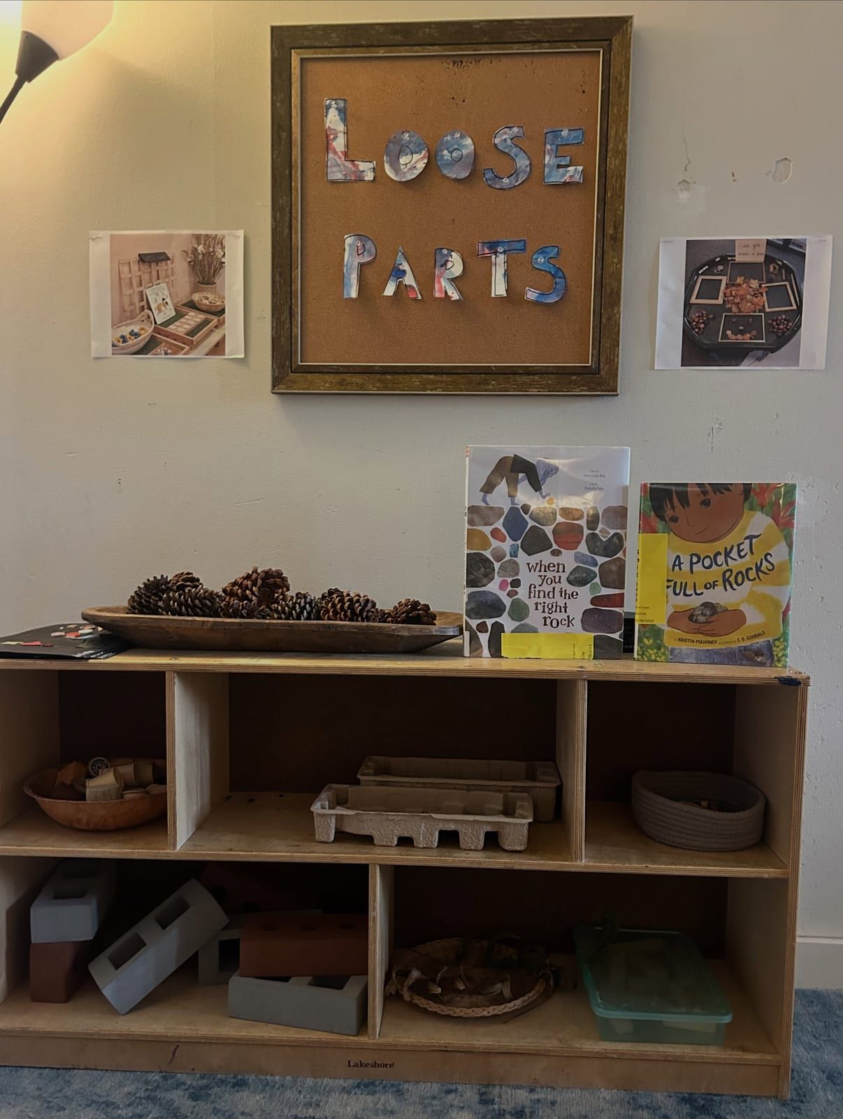 A classroom shelf under a Loose Parts sign, with pinecones, books and baskets of natural materials.