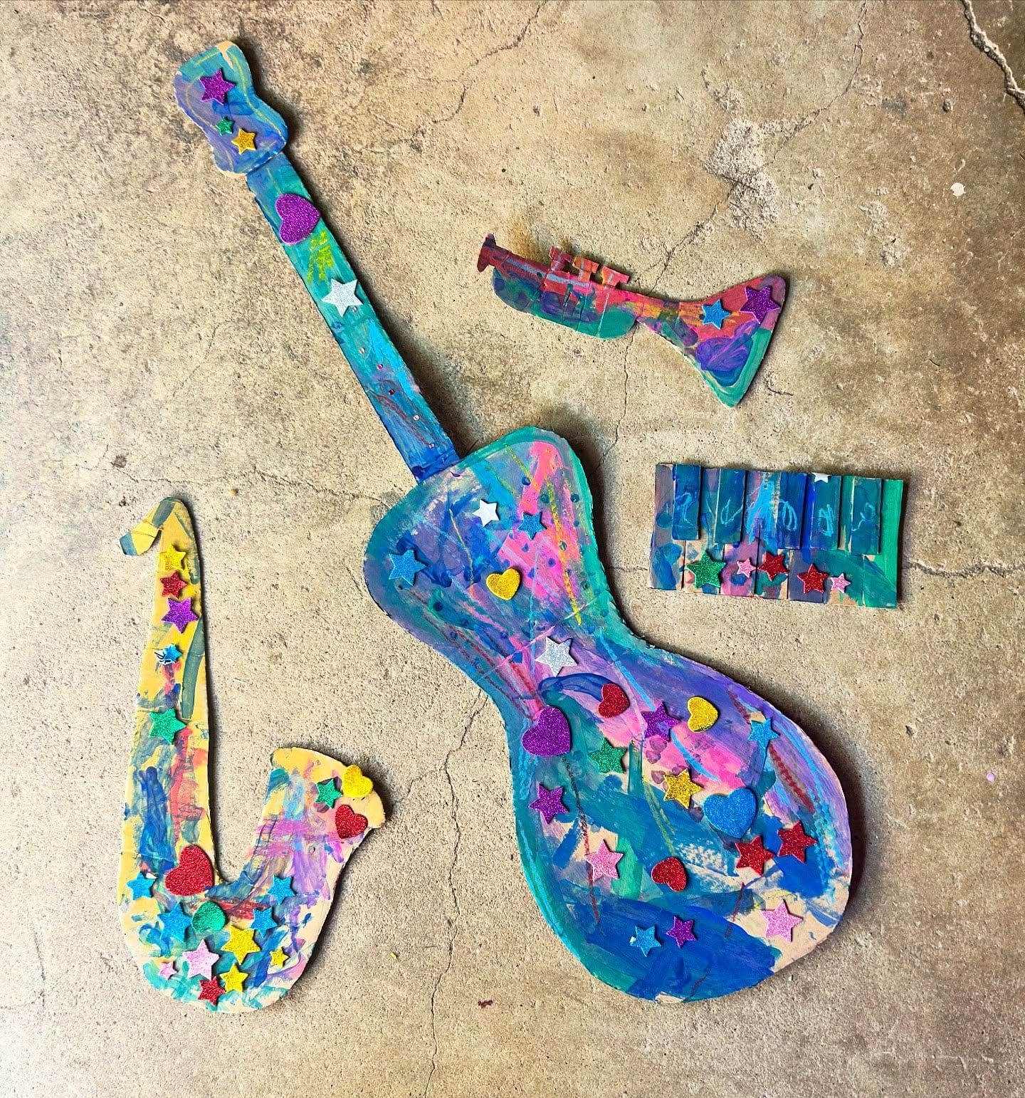 A guitar, a saxophone and a trumpet cut from cardboard and painted in bright colors, decorated with star and heart stickers.