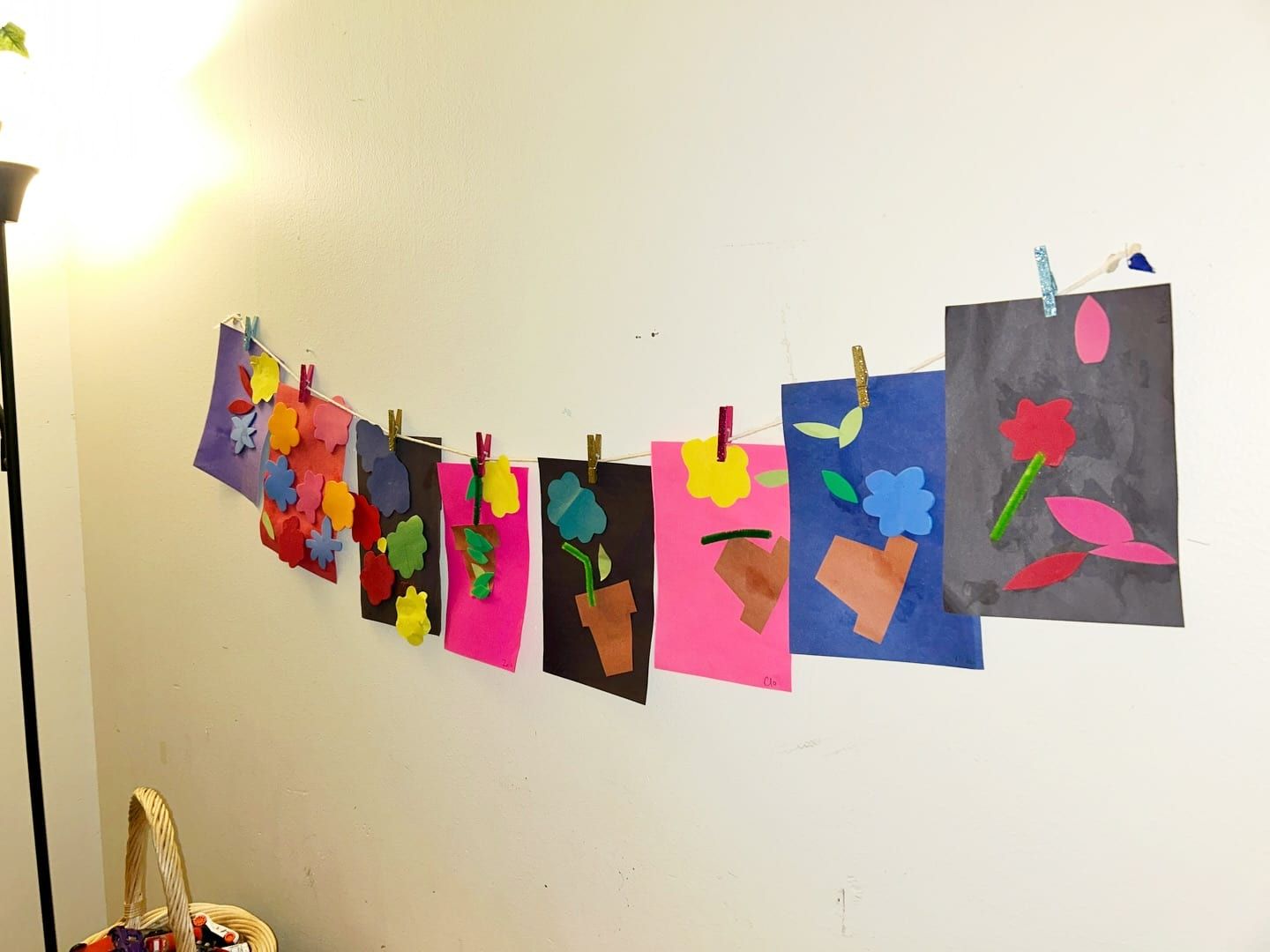 Paper collages of flowers in pots, clipped with clothespins along a line on a classroom wall.